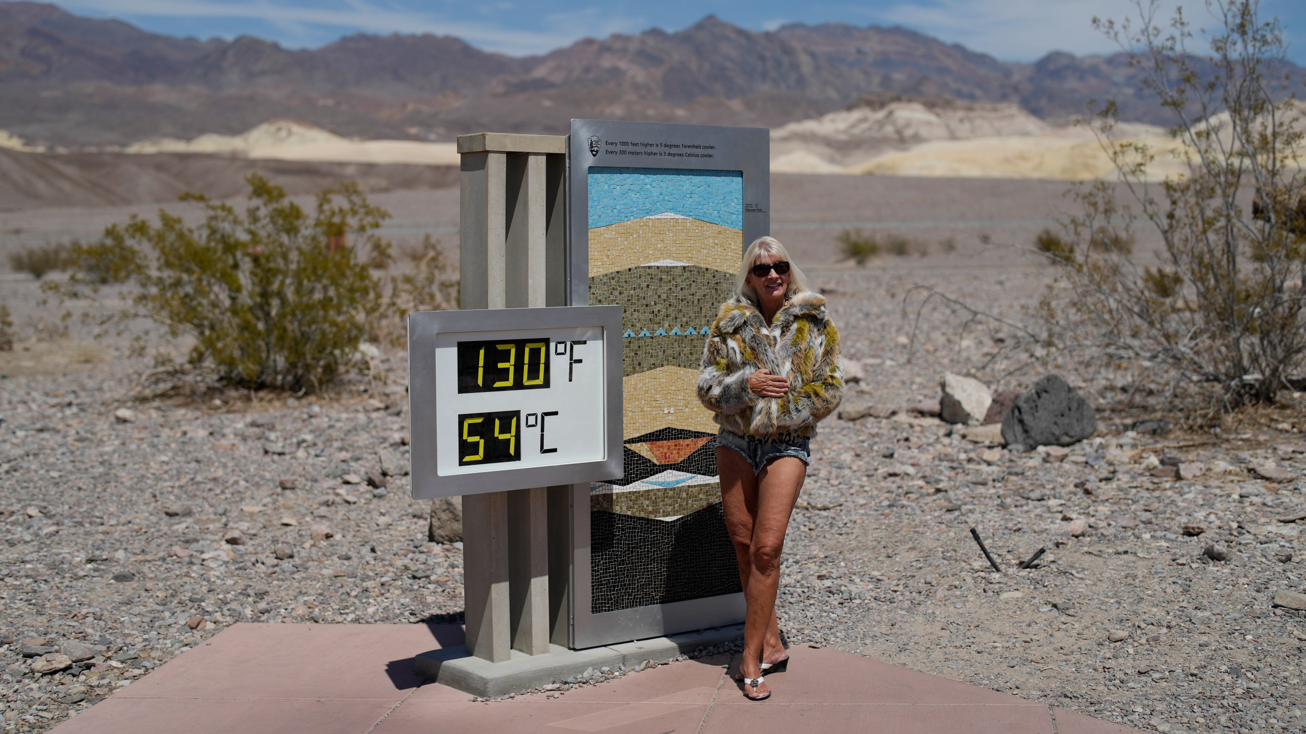 A woman poses by a thermometer, Sunday, July 16, 2023, in Death Valley National Park, Calif. The thermometer is not official but is a popular photo spot. Death Valley's brutal temperatures come amid a blistering stretch of hot weather that has put roughly one-third of Americans under some type of heat advisory, watch or warning. (AP Photo/John Locher)