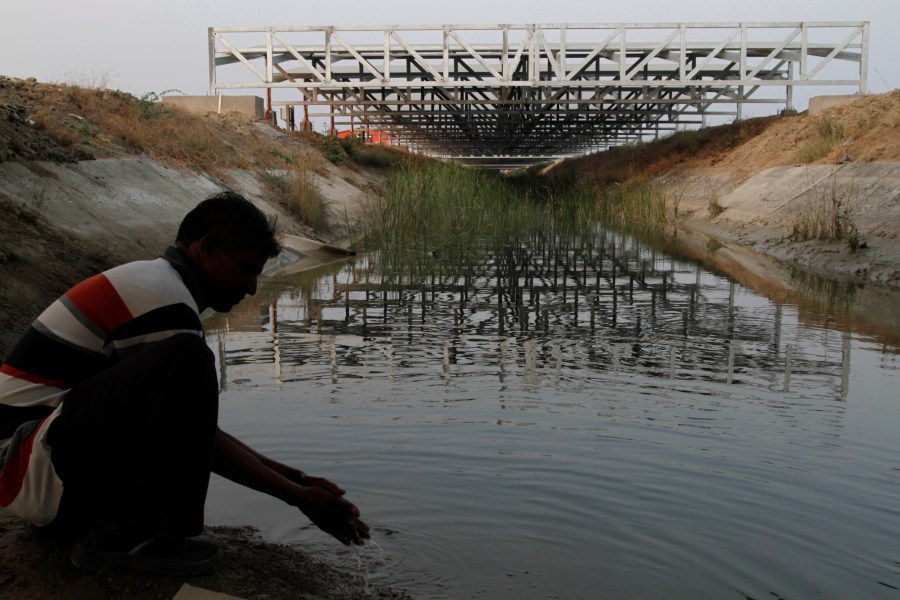 FILE - A worker washes his hands as installed solar panels are visible atop the Narmada canal at Chandrasan village, outside of Ahmadabad, India, Feb. 16, 2012. The project brings water to hundreds of thousands of villages in the dry, arid regions of western India’s Gujarat state. (AP Photo/Ajit Solanki, File)