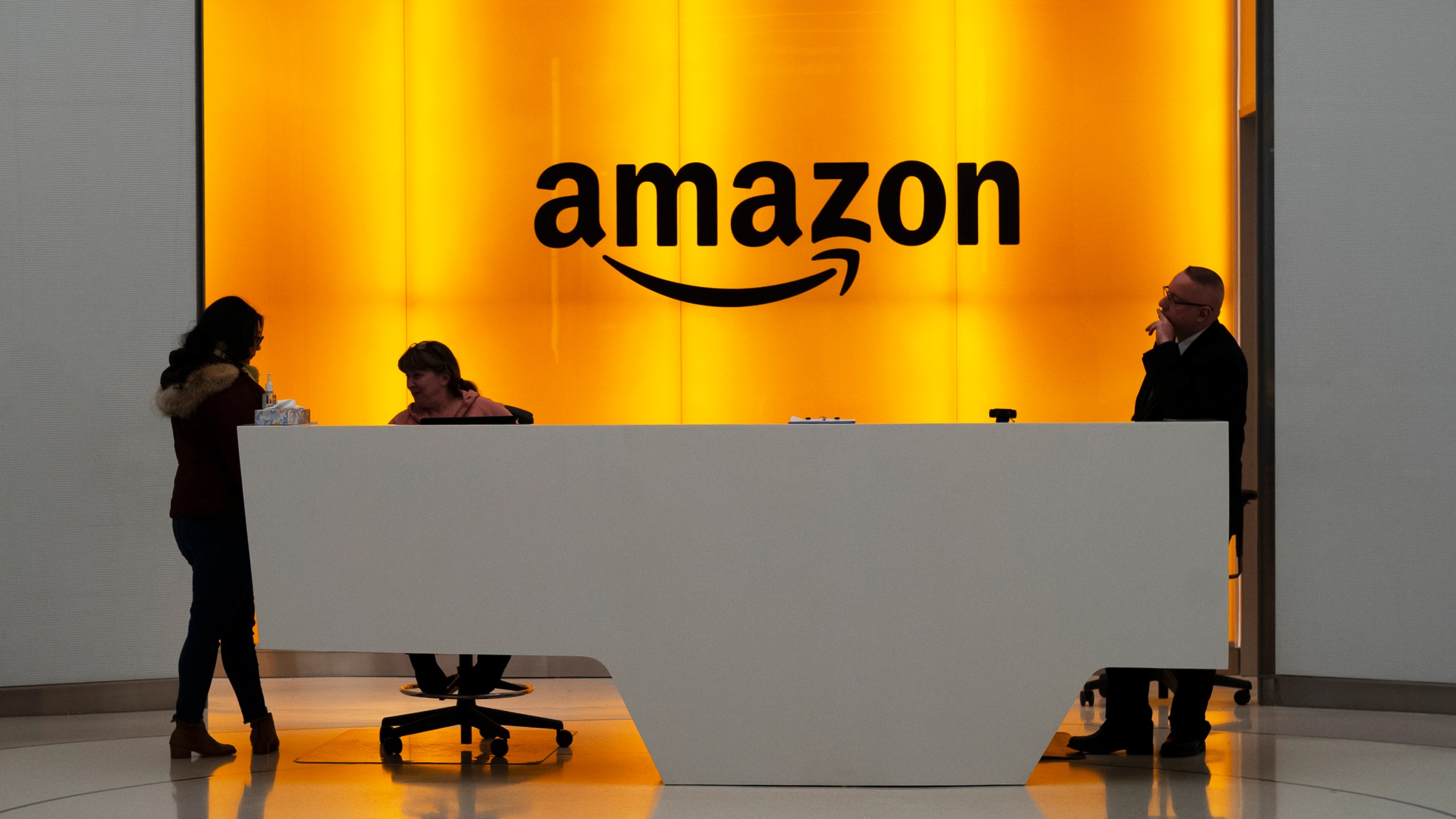 FILE - In this Feb. 14, 2019, file photo, people stand in the lobby for Amazon offices in New York. Amazon is asking some corporate workers to relocate to other cities as part of its return-to-office policy, which mandates workers to be in the office three days a week. (AP Photo/Mark Lennihan, File)