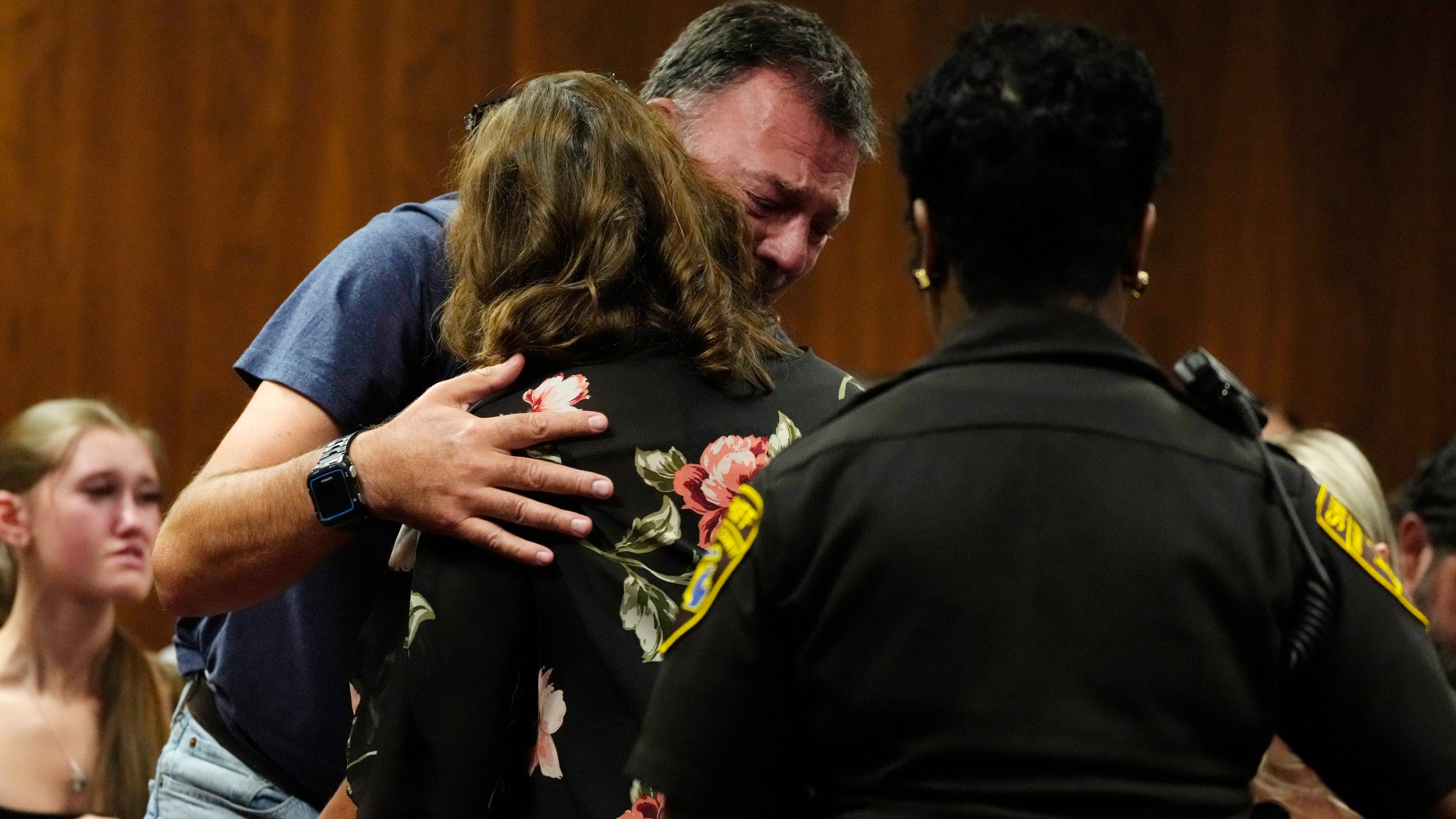 Buck Myre, background, father of slain Oxford student Tate Myre, hugs Assistant Principal Kristy Gibson-Marshall in court, Friday, July 28, 2023, in Pontiac, Mich. Prosecutors are making their case that the Michigan teenager should be sentenced to life in prison for killing four students at his high school in 2021. Prosecutors introduced dark journal entries written by Ethan Crumbley, plus chilling video and testimony from a wounded staff member. (AP Photo/Carlos Osorio)