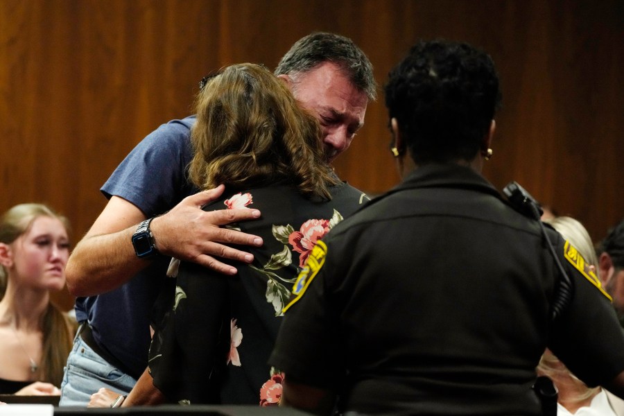 Buck Myre, background, father of slain Oxford student Tate Myre, hugs Assistant Principal Kristy Gibson-Marshall in court, Friday, July 28, 2023, in Pontiac, Mich. Prosecutors are making their case that the Michigan teenager should be sentenced to life in prison for killing four students at his high school in 2021. Prosecutors introduced dark journal entries written by Ethan Crumbley, plus chilling video and testimony from a wounded staff member. (AP Photo/Carlos Osorio)