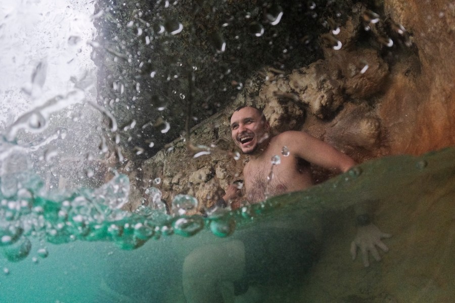 FILE - A young man cools off under a waterfall on a cloudy day with temperatures in the high 80s and intermittent rain storms, during a respite from an ongoing heat wave, at the aquifer-fed Venetian Pool in Coral Gables, Fla., July 27, 2023. Nearly 60% of the U.S. population, are under a heat advisory or flood warning or watch as the high temperatures spread and new areas are told to expect severe storms. (AP Photo/Rebecca Blackwell, File)