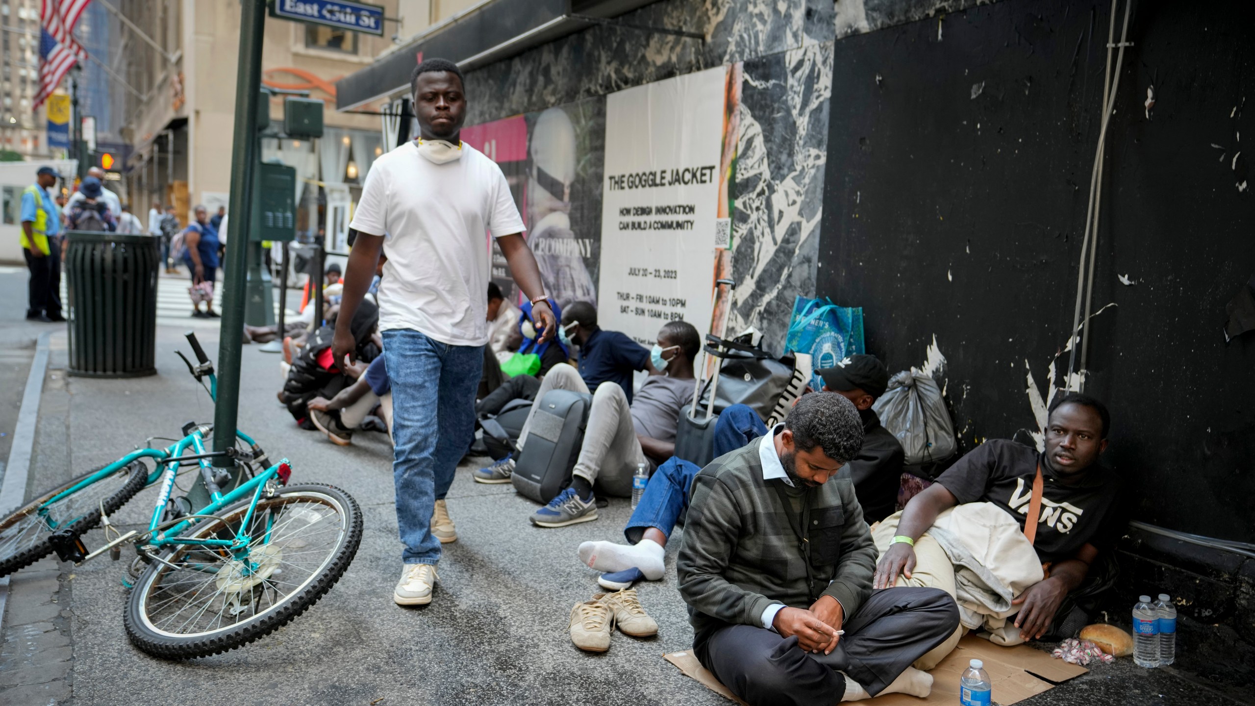 Migrants sit in a queue outside of The Roosevelt Hotel that is being used by the city as temporary housing, Monday, July 31, 2023, in New York. (AP Photo/John Minchillo)