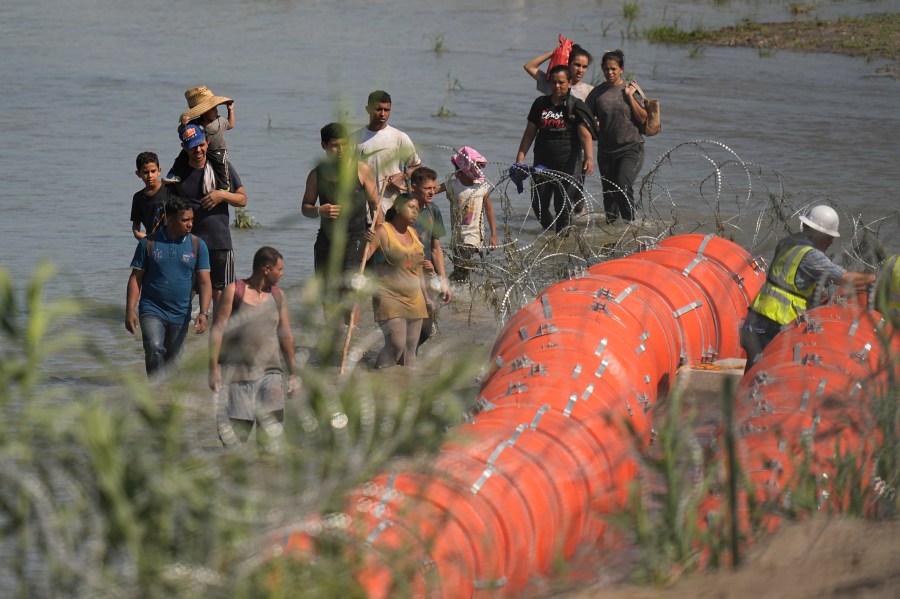 Migrants trying to enter the U.S. from Mexico approach the site where workers are assembling large buoys to be used as a border barrier along the banks of the Rio Grande in Eagle Pass, Texas, Tuesday, July 11, 2023. The floating barrier is being deployed in an effort to block migrants from entering Texas from Mexico. (AP Photo/Eric Gay)