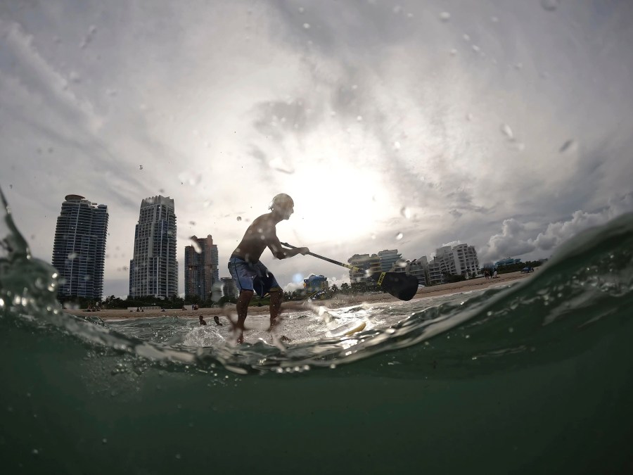 FILE - Graziano La Grasta, a local contractor and paddle board enthusiast, rides a small wave off South Beach, July 28, 2023, in Miami Beach, Fla. Across the U.S., many people are living through one of the most brutal summers of their lives and reckoning with the idea that climate change is only going to make matters worse in the coming decades. (AP Photo/Rebecca Blackwell, File)