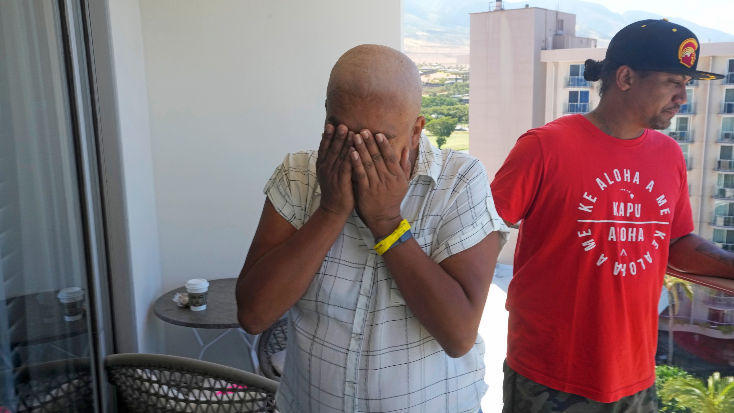 Makalea Ahhee, left, tears up while her husband, JP Mayoga, right, a chef at the Westin Maui, Kaanapali, stand on their balcony at the hotel and resort, Sunday, Aug. 13, 2023, near Lahaina, Hawaii. About 200 employees are living there with their families in the resort. Officials urge tourists to avoid traveling to Maui as many hotels prepare to house evacuees and first responders on the island where a wildfire demolished a historic town and killed dozens of people. (AP Photo/Rick Bowmer)