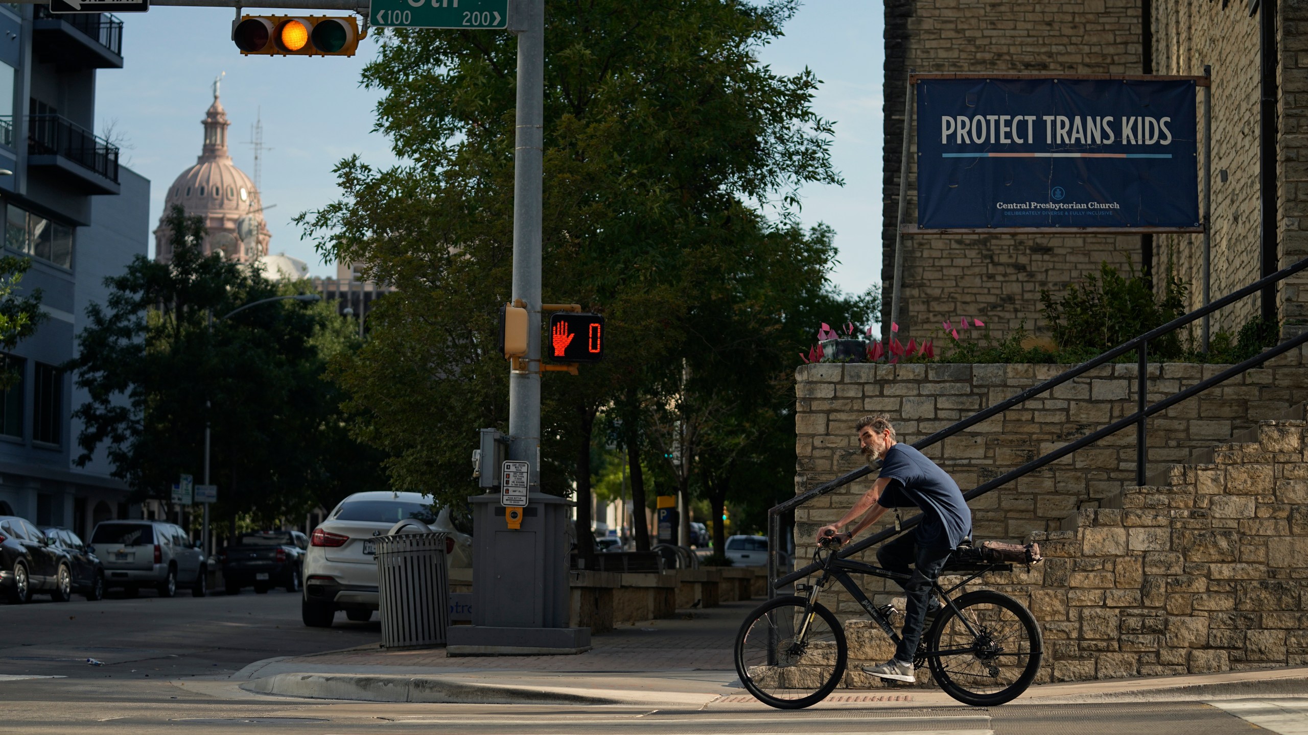 A cyclist passes a sign encouraging the protection of transgender children at Central Presbyterian Church near the Texas Capitol, Tuesday, Aug. 15, 2023, in Austin, Texas. Waiting lists for gender-affirming health care are growing in states that declared themselves refuges for transgender people as bans for such care for minors take effect around the country. Texas, one of the largest states, has a ban that's set to take effect Sept. 1. (AP Photo/Eric Gay)