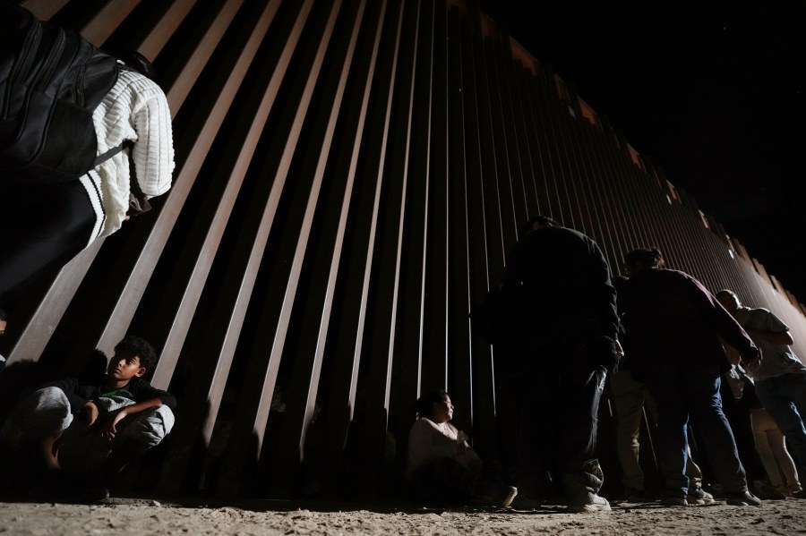 People line up against a border wall as they wait to apply for asylum after crossing the border from Mexico Tuesday, July 11, 2023, near Yuma, Arizona. Thousands of migrants from the north African country of Mauritania have arrived in the U.S. in recent months, following a new route taking them to Nicaragua and up through the southern border. (AP Photo/Gregory Bull)