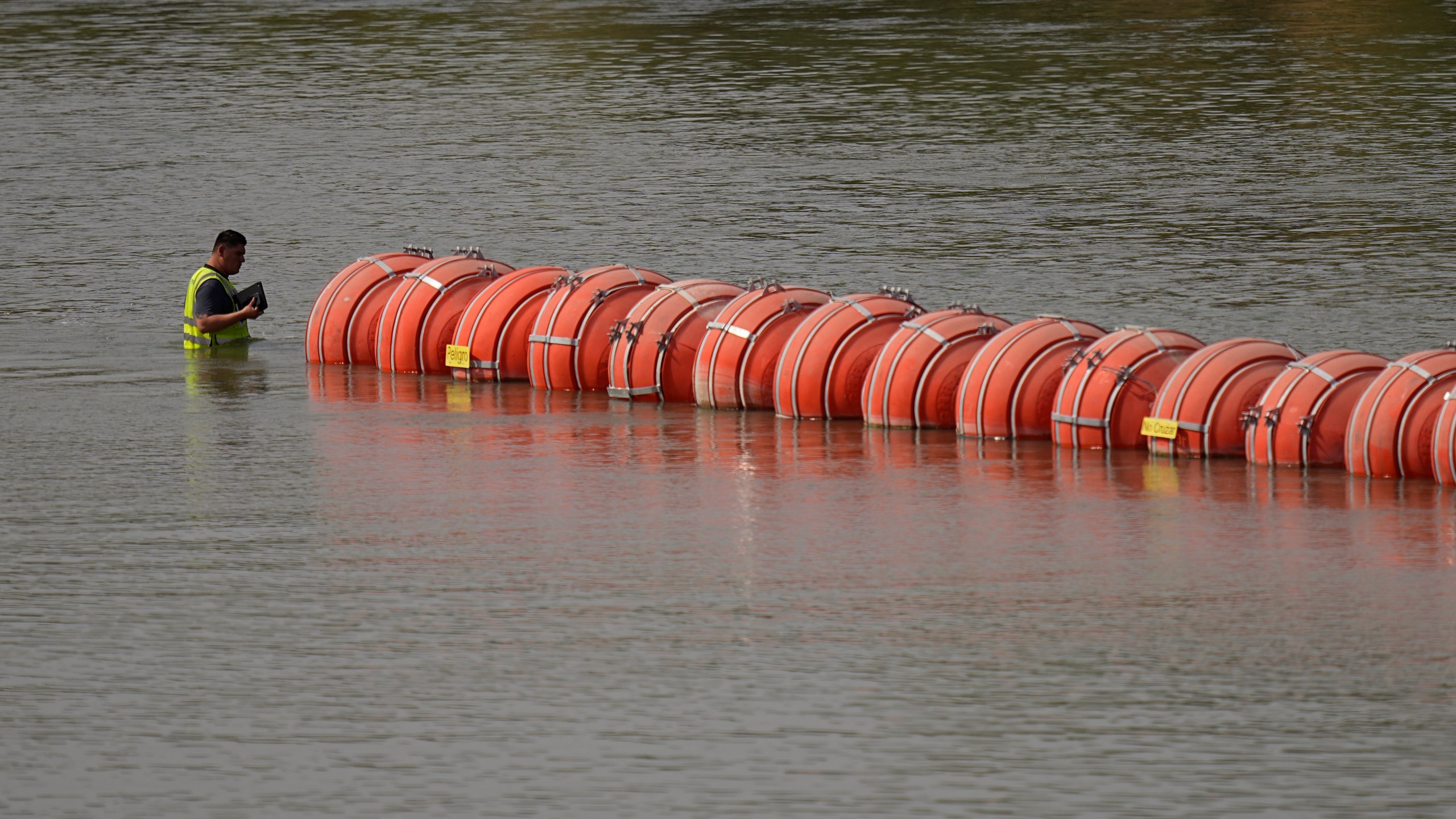 A worker inspects buoys being used as a barrier along the Rio Grande, Monday, Aug. 21, 2023, in Eagle Pass, Texas. (AP Photo/Eric Gay)