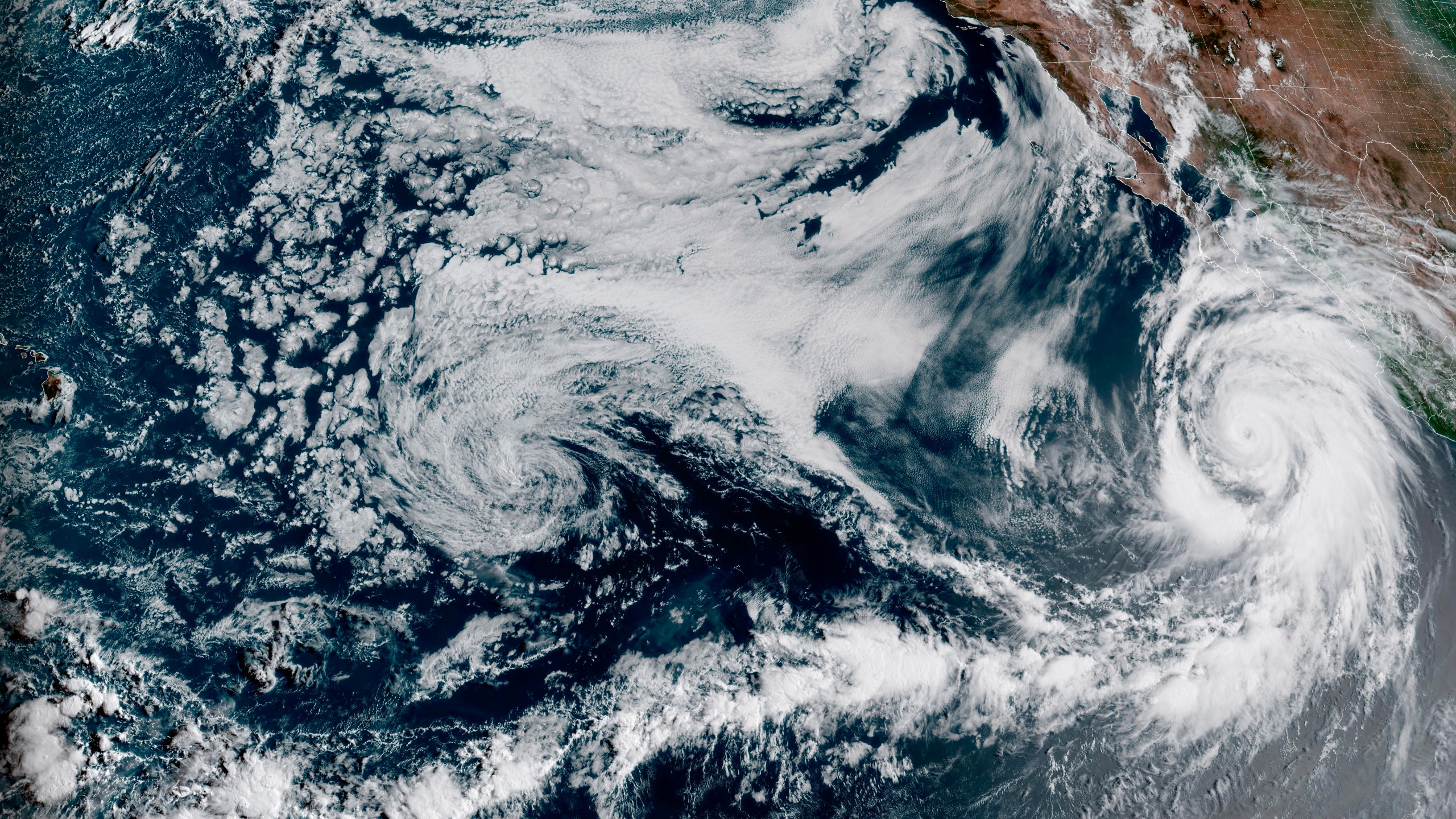 This Friday, Aug. 18, 2023, 1:10 p.m. EDT satellite image provided by the National Oceanic and Atmospheric Administration shows Hurricane Hilary, right, off Mexico's Pacific coast. Scientists figure a natural El Nino, human-caused climate change, a stubborn heat dome over the nation’s midsection and other factors cooked up Hilary’s record-breaking slosh into California and Nevada. (NOAA via AP)