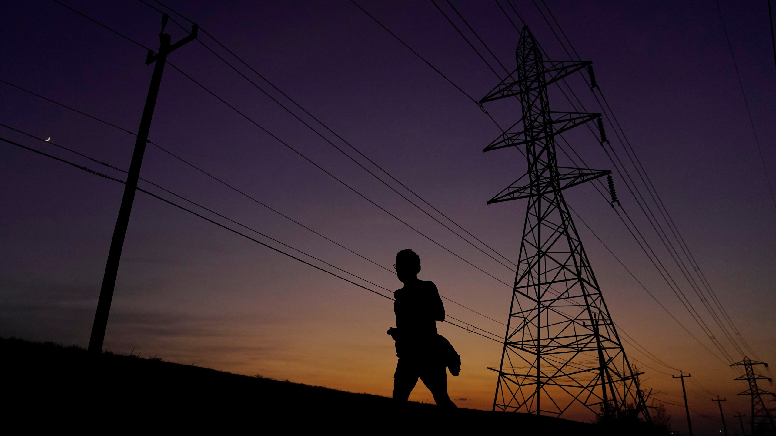 FILE - A jogger passes power lines during a sunset run, Aug. 20, 2023, in San Antonio, as high temperatures continue to stress the power grid. On Thursday, Sept. 7, Texas' power grid manager again asked residents to cut back on electricity as a prolonged and punishing summer heat wave continued, a day after the system was pushed to brink of outages for the first time since a deadly winter blackout in 2021. (AP Photo/Eric Gay, File)