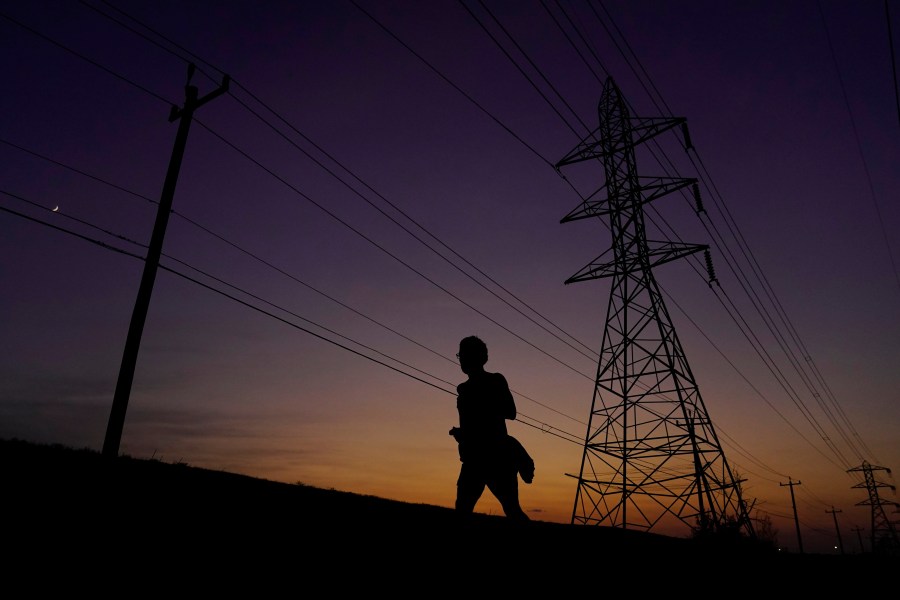 FILE - A jogger passes power lines during a sunset run, Aug. 20, 2023, in San Antonio, as high temperatures continue to stress the power grid. On Thursday, Sept. 7, Texas' power grid manager again asked residents to cut back on electricity as a prolonged and punishing summer heat wave continued, a day after the system was pushed to brink of outages for the first time since a deadly winter blackout in 2021. (AP Photo/Eric Gay, File)