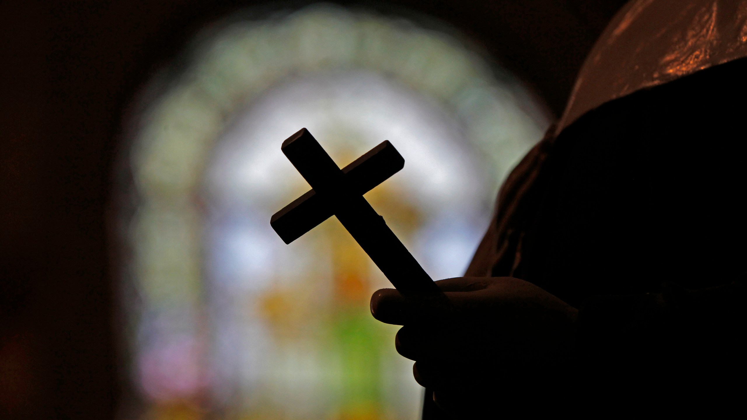 FILE - This Dec. 1, 2012 file photo shows a silhouette of a crucifix and a stained glass window inside a Catholic Church in New Orleans. On Thursday, Sept. 7, 2023, a Louisiana state grand jury charged a now-91-year-old disgraced priest, Lawrence Hecker, with sexually assaulting a teenage boy in 1975, an extraordinary prosecution that could shed new light on what Roman Catholic Church leaders knew about a child sex abuse crisis that persisted for decades and claimed hundreds of victims. (AP Photo/Gerald Herbert, File)