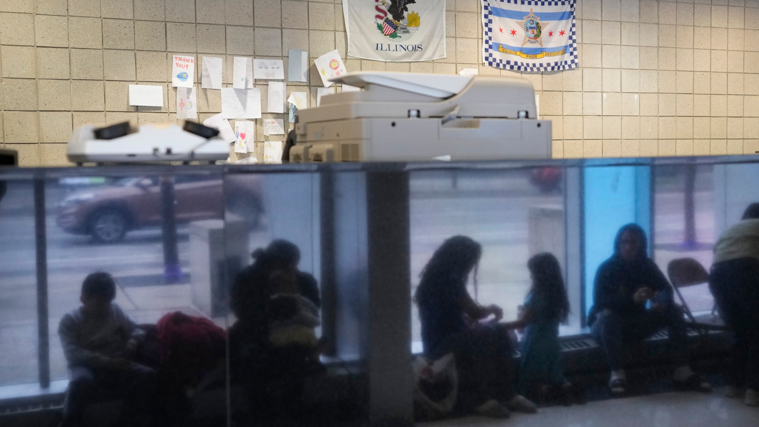 FILE - Immigrants from Venezuela are reflected in a marble wall while taking shelter at the Chicago Police Department's 16th District station on Monday, May 1, 2023. Nearly 1,600 migrants seeking asylum in the U.S. will be relocated from Chicago police stations to winterized camps with massive tents under a plan by Mayor Brandon Johnson, according to a report released Thursday, Sept. 7, 2023. (AP Photo/Charles Rex Arbogast, FIle)