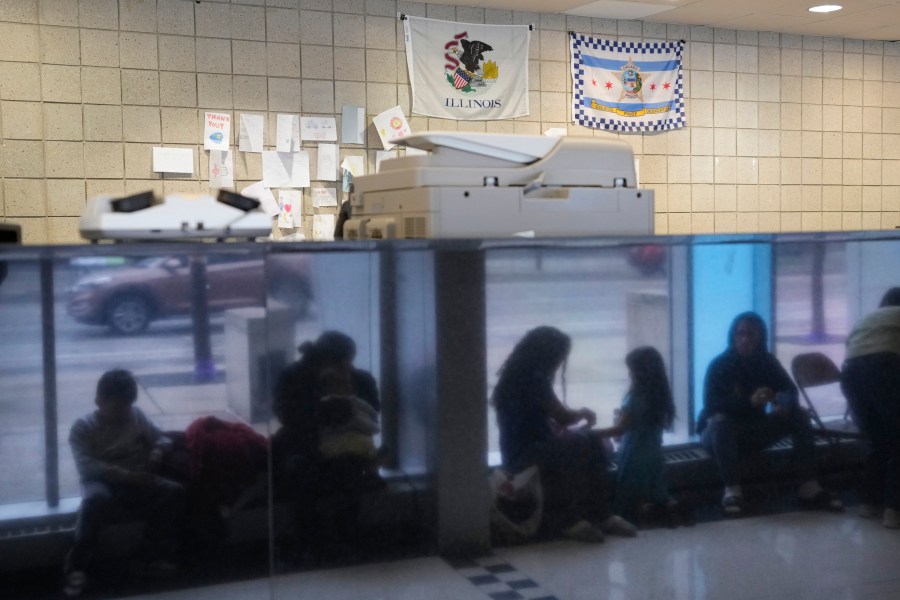 FILE - Immigrants from Venezuela are reflected in a marble wall while taking shelter at the Chicago Police Department's 16th District station on Monday, May 1, 2023. Nearly 1,600 migrants seeking asylum in the U.S. will be relocated from Chicago police stations to winterized camps with massive tents under a plan by Mayor Brandon Johnson, according to a report released Thursday, Sept. 7, 2023. (AP Photo/Charles Rex Arbogast, FIle)