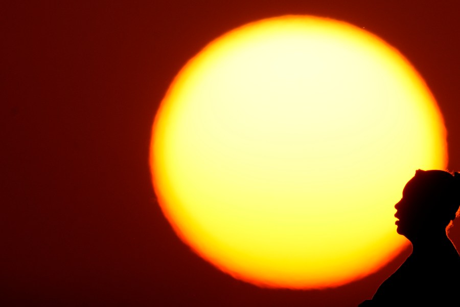 FILE - A woman is silhouetted against the setting sun as triple-digit heat indexes continue in the Midwest, Aug. 20, 2023, in Kansas City, Mo. Earth is exceeding its “safe operating space for humanity” in six of nine key measurements of its health, and two of the remaining three are headed in the wrong direction, a new study said. (AP Photo/Charlie Riedel, File)