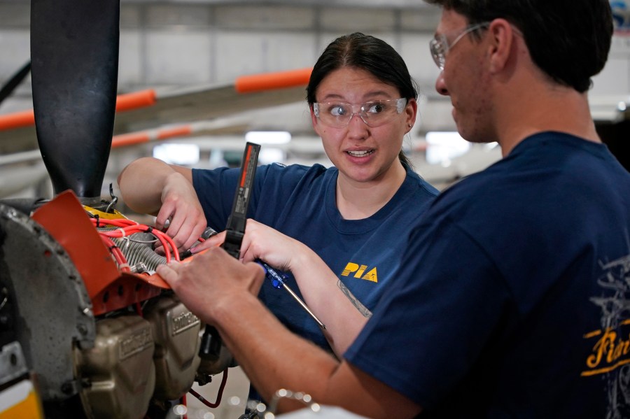 File - Students at the Pittsburgh Institute of Aeronautics Nikki Reed, center, and William Onderdork study the engine on an Cessna 310 aircraft in West Mifflin, Pa., May 2, 2023. On Friday, the U.S. government issues its latest monthly jobs report. (AP Photo/Gene J. Puskar, File)