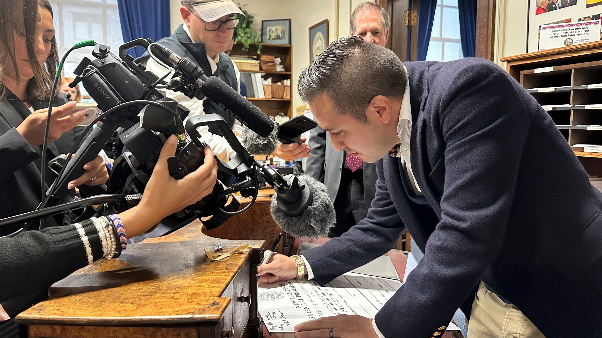 John Anthony Castro, of Texas, signs a commemorative poster after filing to get on the Republican ballot for the 2024 New Hampshire primary in Concord, N.H., on Wednesday, Oct. 11, 2023. Castro, who has filed multiple lawsuits contending the 14th Amendment bars former President Donald Trump's candidacy, wrote: "Freedom comes from our Constitution. Without that we fall." (AP Photo/Holly Ramer)