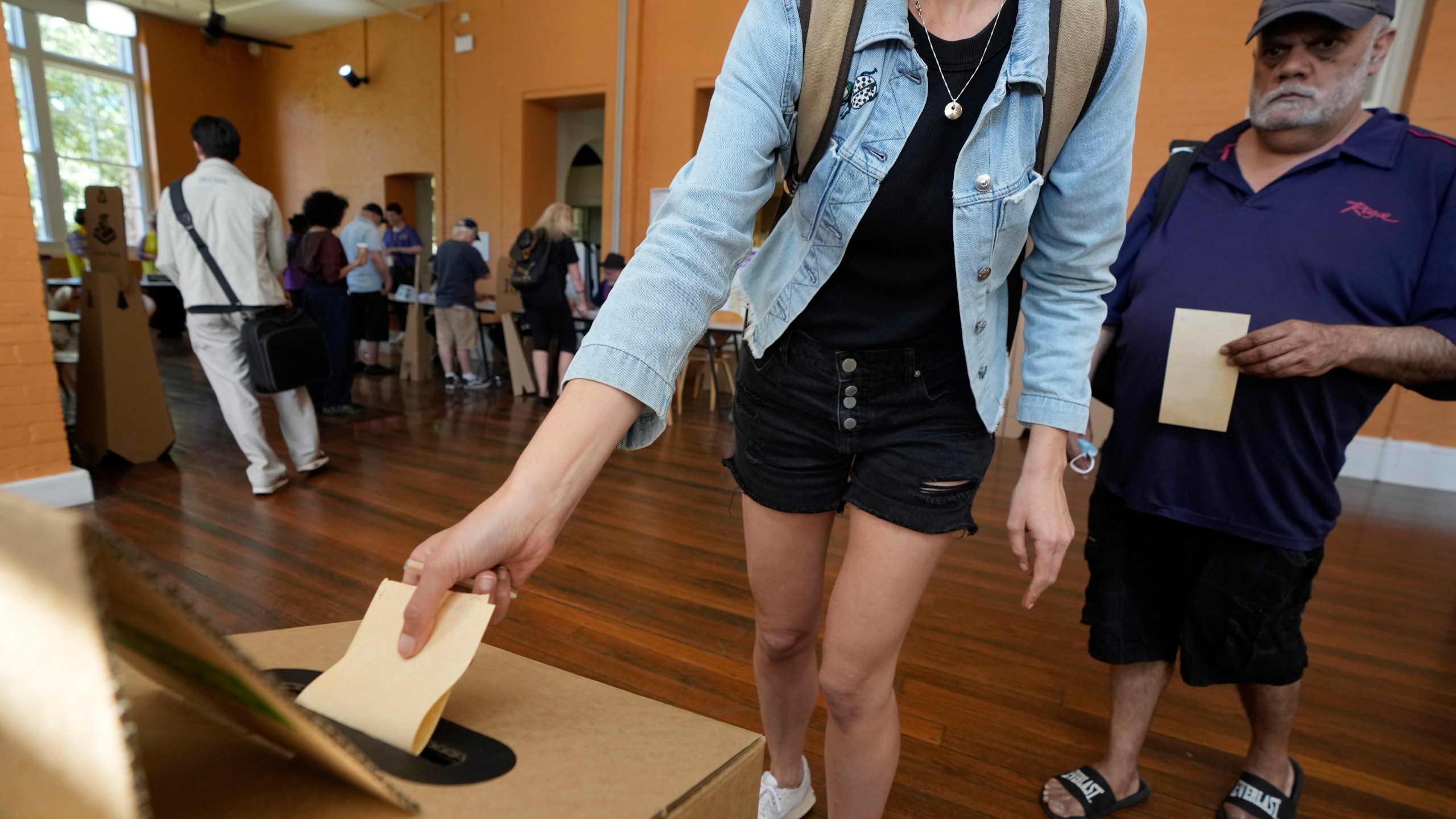 A man, right, waits as a woman drops her ballot into a box a polling place in Redfern as Australians cast their final votes in Sydney, Saturday, Oct. 14, 2023, in their first referendum in a generation that aims to tackle Indigenous disadvantage by enshrining in the constitution a new advocacy committee. Australia will look for new ways to lift Indigenous living standards after voters soundly rejected a proposal to create a new advocacy committee, the deputy prime minister said on Sunday, Oct. 15. (AP Photo/Rick Rycroft, File)