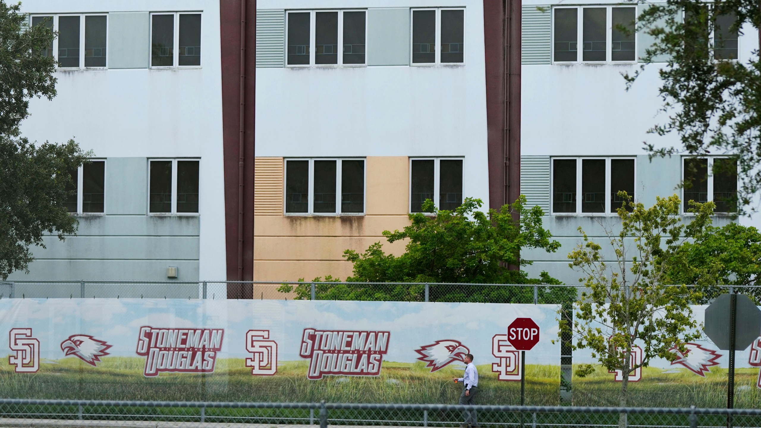 FILE - A security agent walks alongside a barrier surrounding Marjory Stoneman Douglas High School, July 5, 2023, in Parkland, Fla. Florida lawmakers and others on Saturday, Oct. 14, toured the school's 1200 Building, where a former student shot 17 people to death and wounded 17 others on Valentine's Day in 2018. The local school district has announced the 1200 Building will be demolished during the summer of 2024. (AP Photo/Rebecca Blackwell, File)
