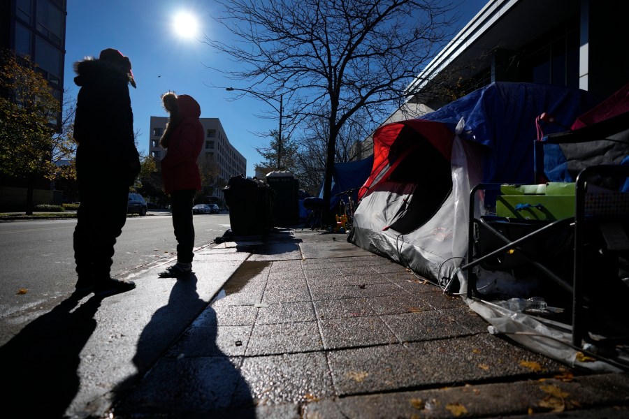 A man and woman stand in the late morning sun near their tent in a small migrant community Wednesday, Nov. 1, 2023, near a Northside police station in Chicago. (AP Photo/Charles Rex Arbogast)