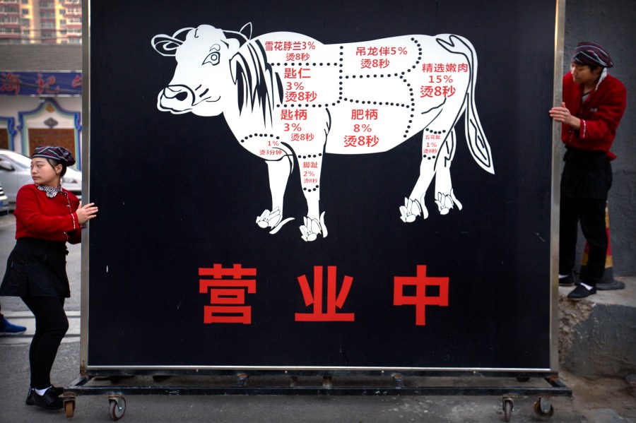 FILE - Restaurant workers move a sign advertising the grand opening of a beef hotpot restaurant along a street in Beijing, Thursday, Oct. 12, 2017. Experts agree that the urgency of climate change and the demands of a surging global population call for an overhaul of how humans get their protein. (AP Photo/Mark Schiefelbein, File)