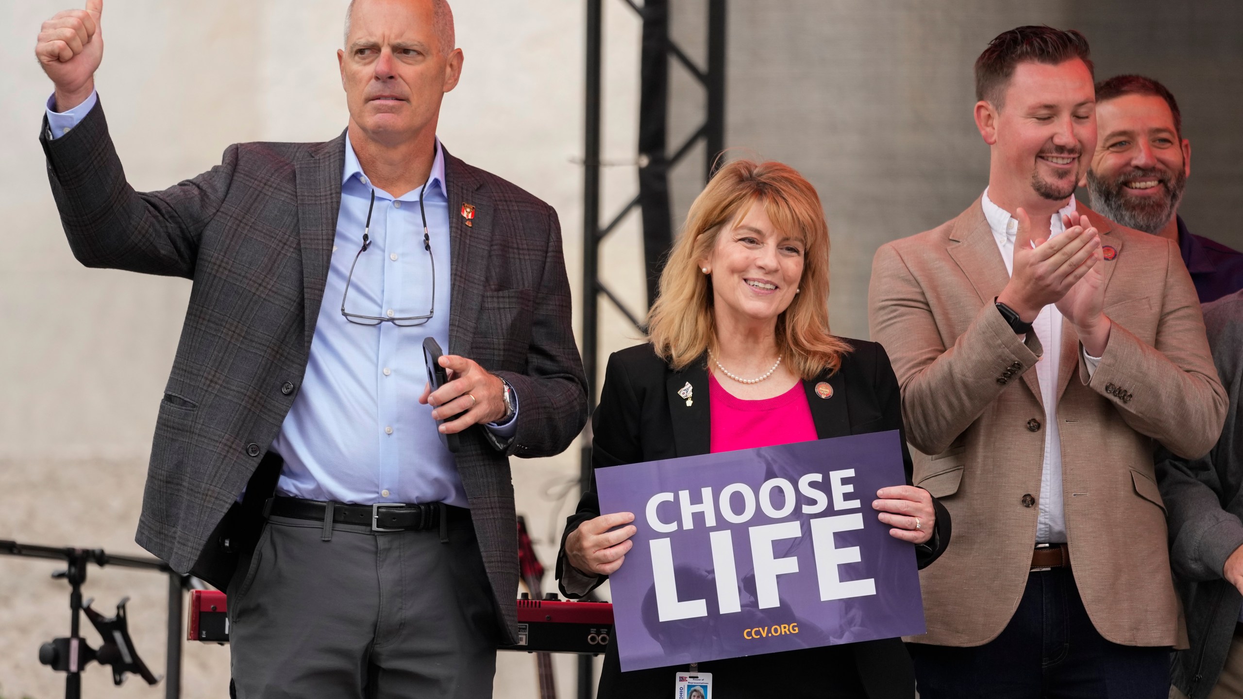 Ohio State Rep. Jennifer Gross, R-West Chester, holding a "Choose Life" sign, center, joined by Ohio State Rep. Adam Bird, R-New Richmond, left, and Ohio State Rep. Thomas Hall, R-Madison Township, right, stand together on stage during the Ohio March for Life rally at the Ohio State House in Columbus, Ohio, Oct. 6, 2023. The statewide battles over abortion rights that have erupted since the U.S. Supreme Court overturned a constitutional right to the procedure have exposed another fault line: commitment to democracy. (AP Photo/Carolyn Kaster)