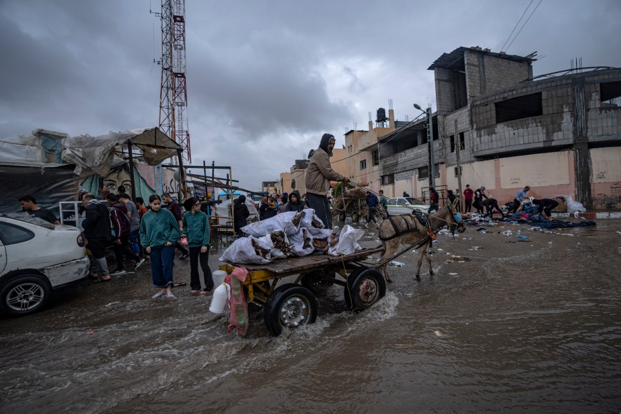 Palestinians displaced by the Israeli bombardment of the Gaza Strip walk through the flooded street after rainfall next to a U.N. displacement camp in the southern town of Khan Younis, Gaza Strip, Sunday, Nov. 19, 2023. Hundreds of thousands of Palestinians have fled their homes in northern Gaza as Israel moves ahead with a ground offensive against the ruling Hamas militant group. (AP Photo/Fatima Shbair)