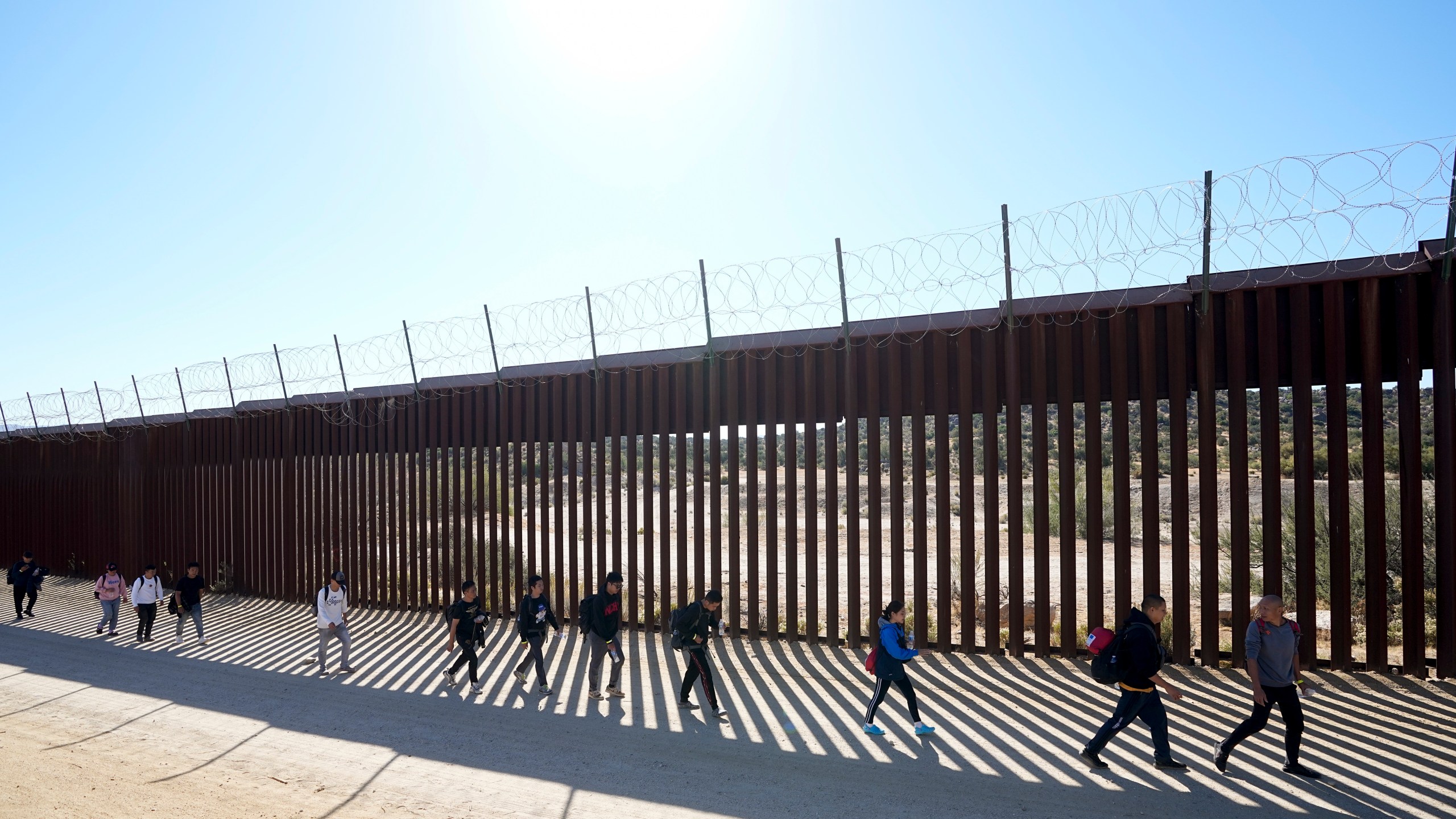 FILE - A group of people, including many from China, walk along the wall after crossing the border with Mexico to seek asylum, Tuesday, Oct. 24, 2023, near Jacumba, Calif. As Congress returns this week, Senate Republicans have made it clear they won’t support additional war aid for Ukraine unless they can pair it with border security measures. (AP Photo/Gregory Bull, File)