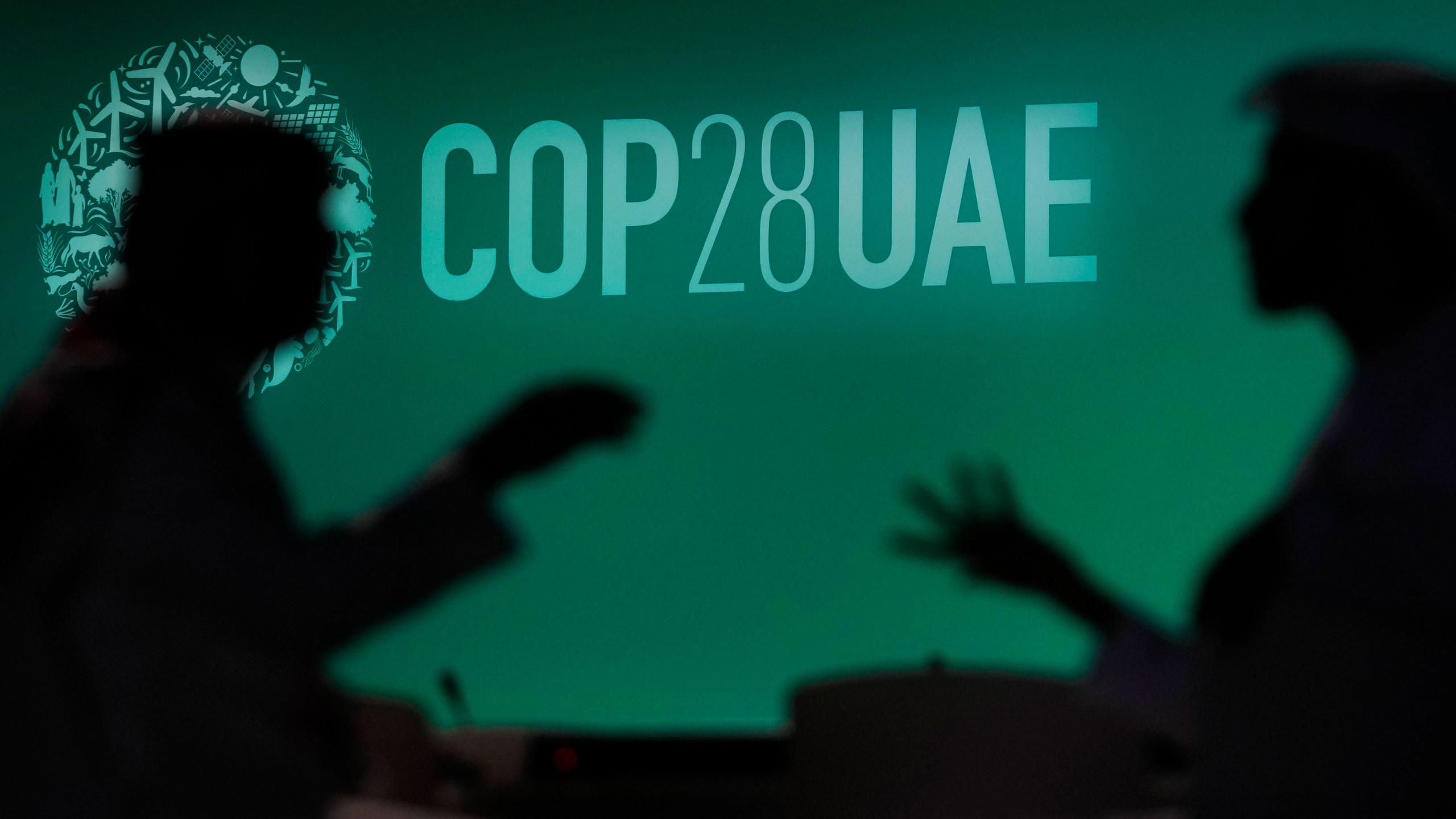 FILE - People are silhouetted against a logo for the COP28 U.N. Climate Summit, Nov. 29, 2023, in Dubai, United Arab Emirates. (AP Photo/Rafiq Maqbool, File)