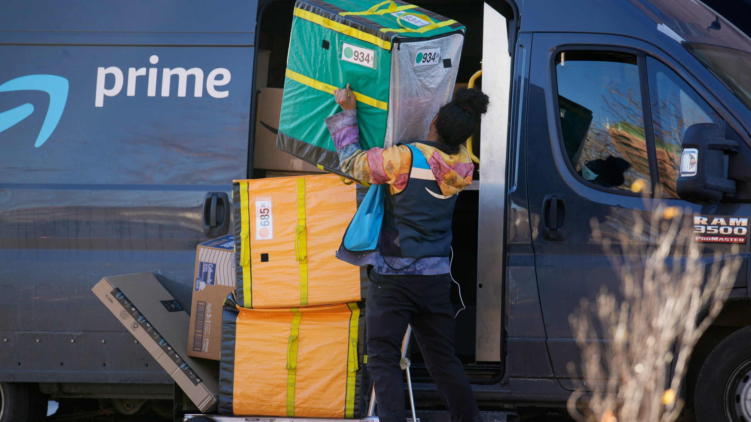 An Amazon Prime delivery person struggles with packages while making a stop at a high-rise apartment building on Tuesday, Nov. 28, 2023, in Denver. (AP Photo/David Zalubowski)