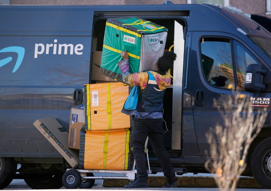 An Amazon Prime delivery person struggles with packages while making a stop at a high-rise apartment building on Tuesday, Nov. 28, 2023, in Denver. (AP Photo/David Zalubowski)