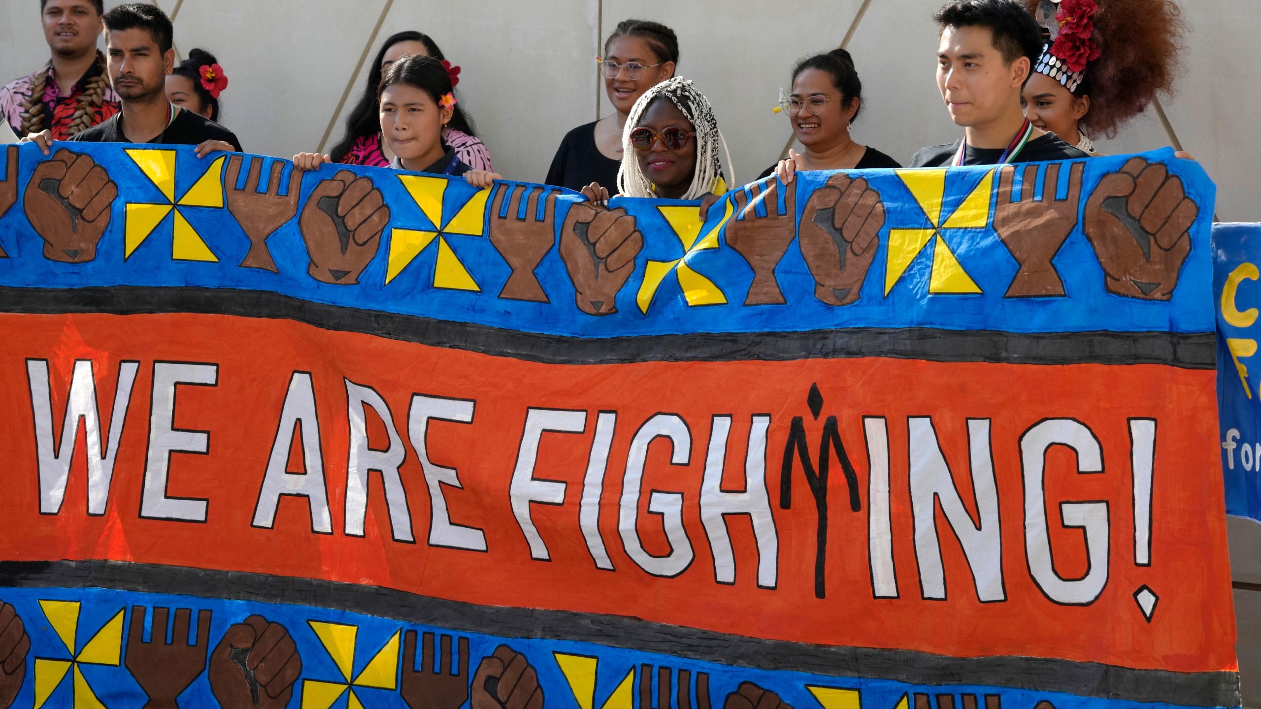 Activists hold a banner reading "we are fighting" at the COP28 U.N. Climate Summit, Friday, Dec. 8, 2023, in Dubai, United Arab Emirates. (AP Photo/Peter Dejong)