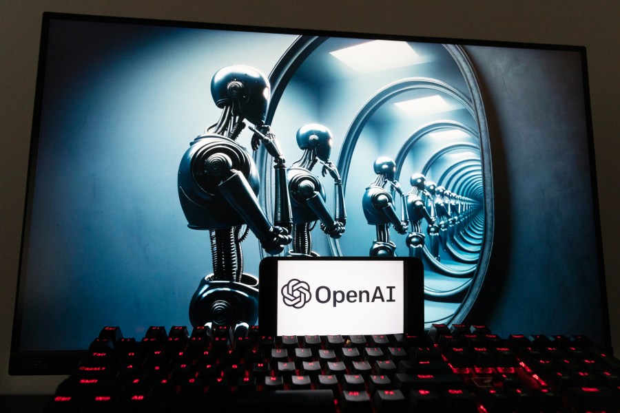 The OpenAI logo is seen displayed on a cell phone with an image on a computer screen generated by ChatGPT's Dall-E text-to-image model, Friday, Dec. 8, 2023, in Boston. Artificial intelligence went mainstream in 2023 — it was a long time coming and has a long way to go for the technology to match people's science fiction fantasies of human-like machines. (AP Photo/Michael Dwyer)