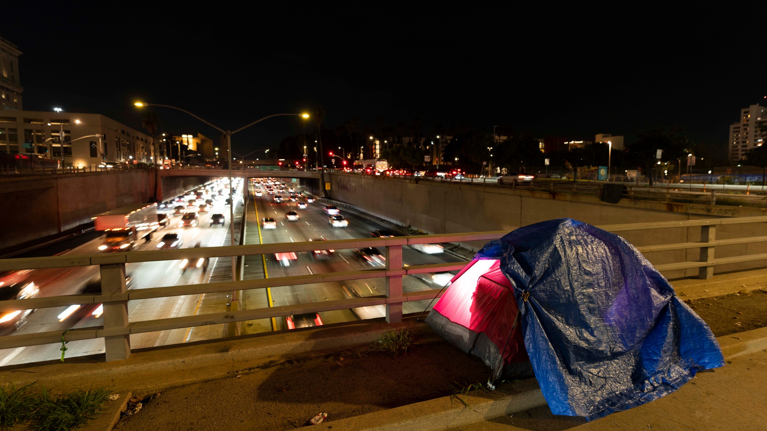 FILE - In this photo illuminated by an off-camera flash, a tarp covers a portion of a homeless person's tent on a bridge overlooking the 101 Freeway in Los Angeles, Thursday, Feb. 2, 2023. The United States experienced a dramatic 12% increase in homelessness as soaring rents and a decline in coronavirus pandemic assistance combined to put housing out of reach for more Americans, federal officials said Friday, Dec. 15, 2023. (AP Photo/Jae C. Hong, File)