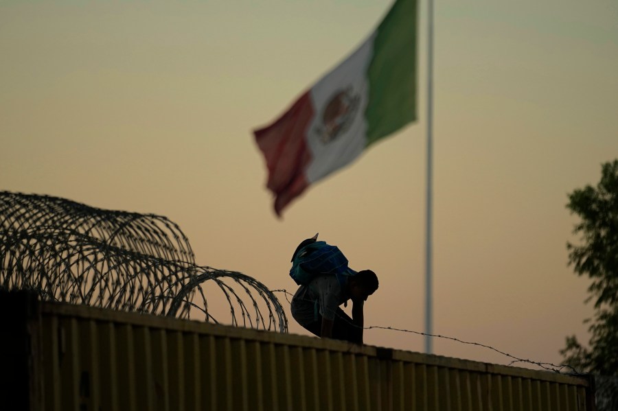 FILE - A migrant who crossed the Rio Grande from Mexico to the U.S. works their way through and over concertina wire and box car barriers, Friday, Sept. 22, 2023, in Eagle Pass, Texas. Abbott is expected to sign into law sweeping new powers that allow police to arrest migrants who cross the border illegally and gives local judges authority to order them to leave the country.(AP Photo/Eric Gay, File)