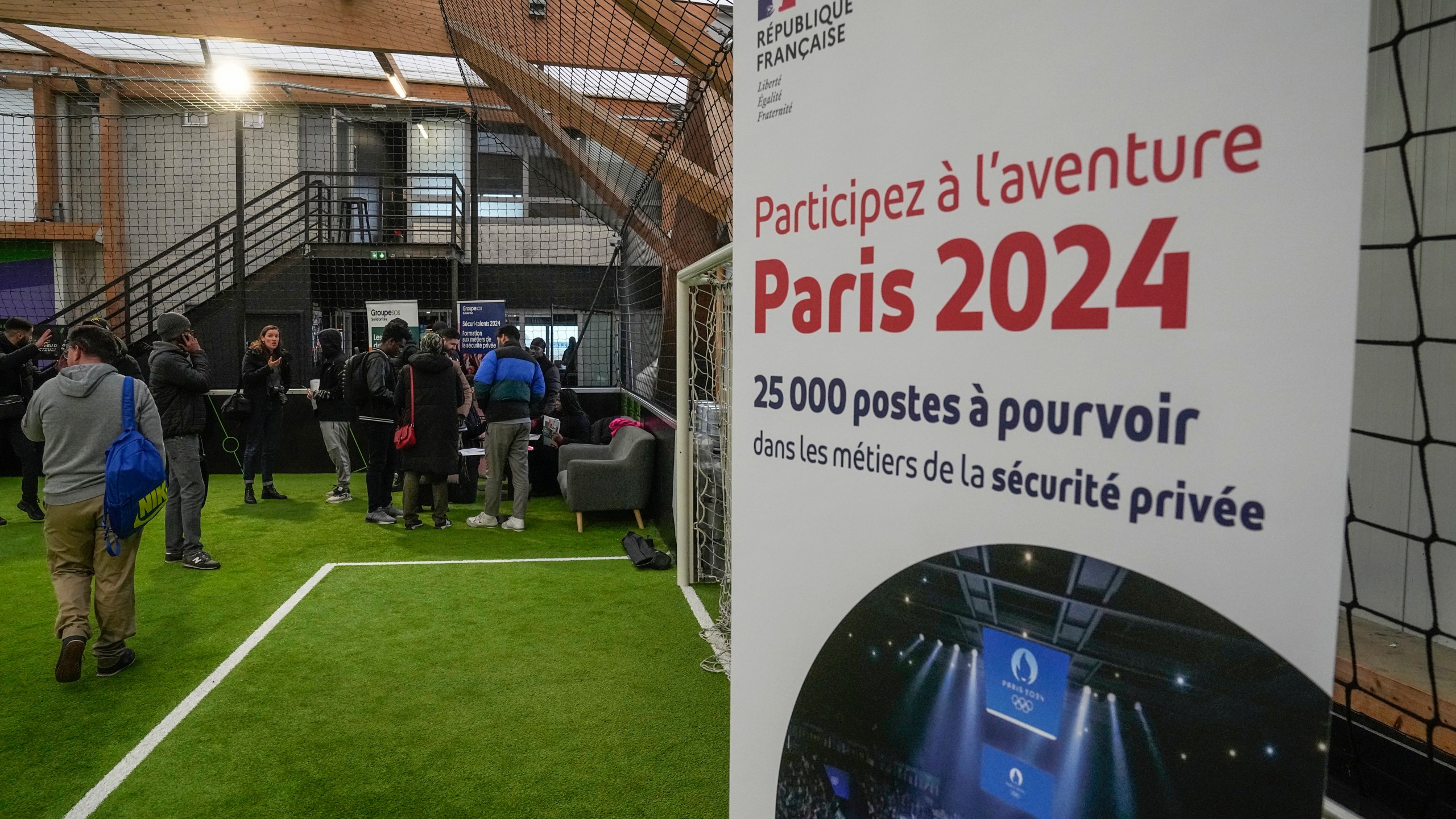 Job seekers line up to get the application papers during the Olympics jobs fair at sport center in Paris, Thursday, Dec. 14, 2023. Organizers urgently need many thousands of recruits for the huge security operation that will aim to keep athletes and spectators safe during the July 26-Aug. 11 Summer Games in the French capital that has been repeatedly hit by deadly extremist attacks. Placard reads, take part in the Paris 2024 adventure, 25,000 jobs to be filled. (AP Photo/Michel Euler)