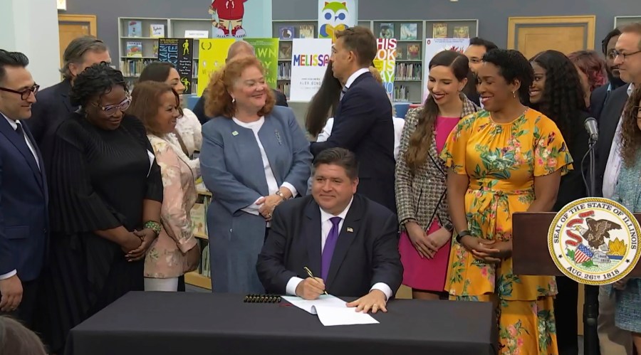 FILE - In this screenshot from a livestream broadcast by the State of Illinois, Gov. J.B. Pritzker signs a bill, June 12, 2023, at Harold Washington Library's Thomas Hughes Children's Library in downtown Chicago. The law will require the state's libraries to uphold a pledge not to ban material because of partisan disapproval, starting Monday, Jan. 1, 2024. If they refuse, they will not receive state funding. (State of Illinois via AP, File)