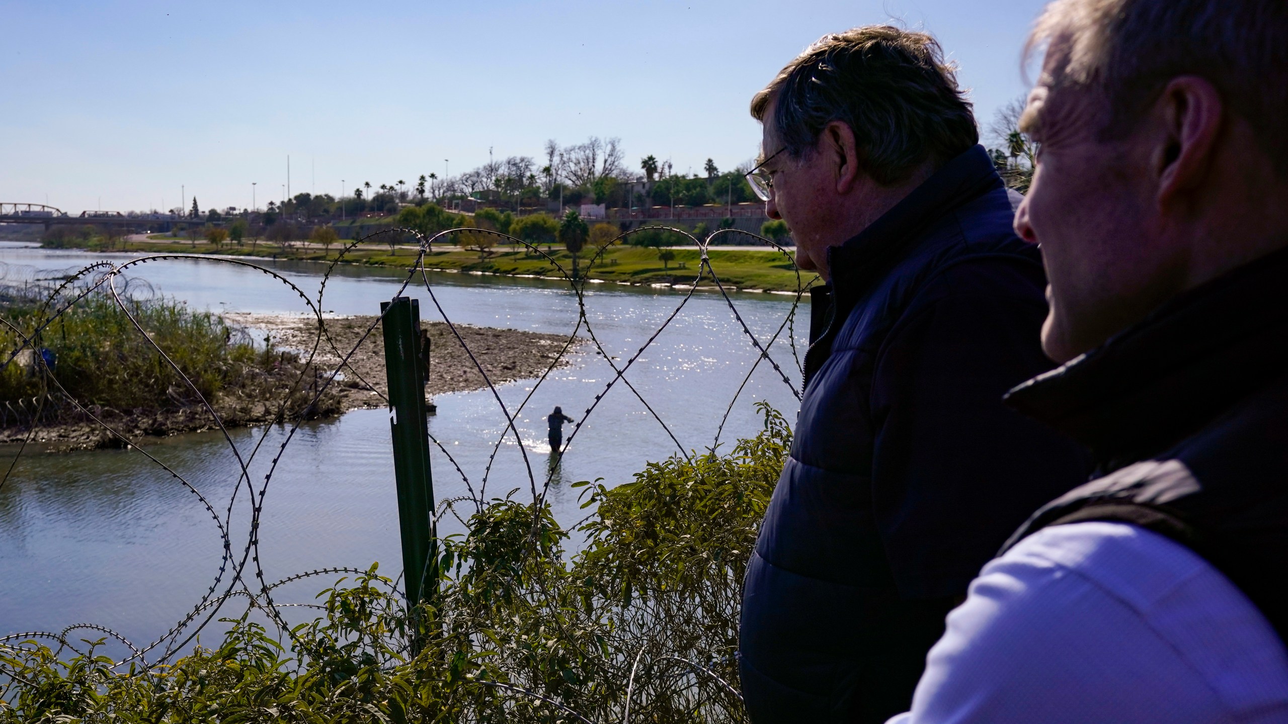 Republican members of Congress look on as migrants cross the Rio Grande at the Texas-Mexico border, Wednesday, Jan. 3, 2024, in Eagle Pass, Texas. U.S. House Speaker Mike Johnson is leading about 60 fellow Republicans in Congress on a visit to the Mexican border. Their trip comes as they are demanding hard-line immigration policies in exchange for backing President Joe Biden's emergency wartime funding request for Ukraine. (AP Photo/Eric Gay)