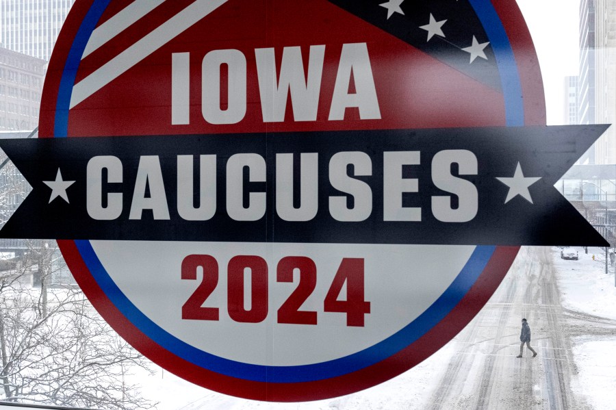 A man walks across the street below a sign for the Iowa Caucuses in downtown Des Moines, Iowa, Saturday, Jan. 13, 2024. (AP Photo/Andrew Harnik)