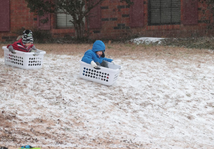 Cannon Lambert, 6, left, and Edward Nahar, 7, race down a hill using laundry baskets for sleds, Monday, Jan. 15, 2024, in Tupelo, Miss., as they enjoy the snowy conditions. (Thomas Wells/The Northeast Mississippi Daily Journal via AP)