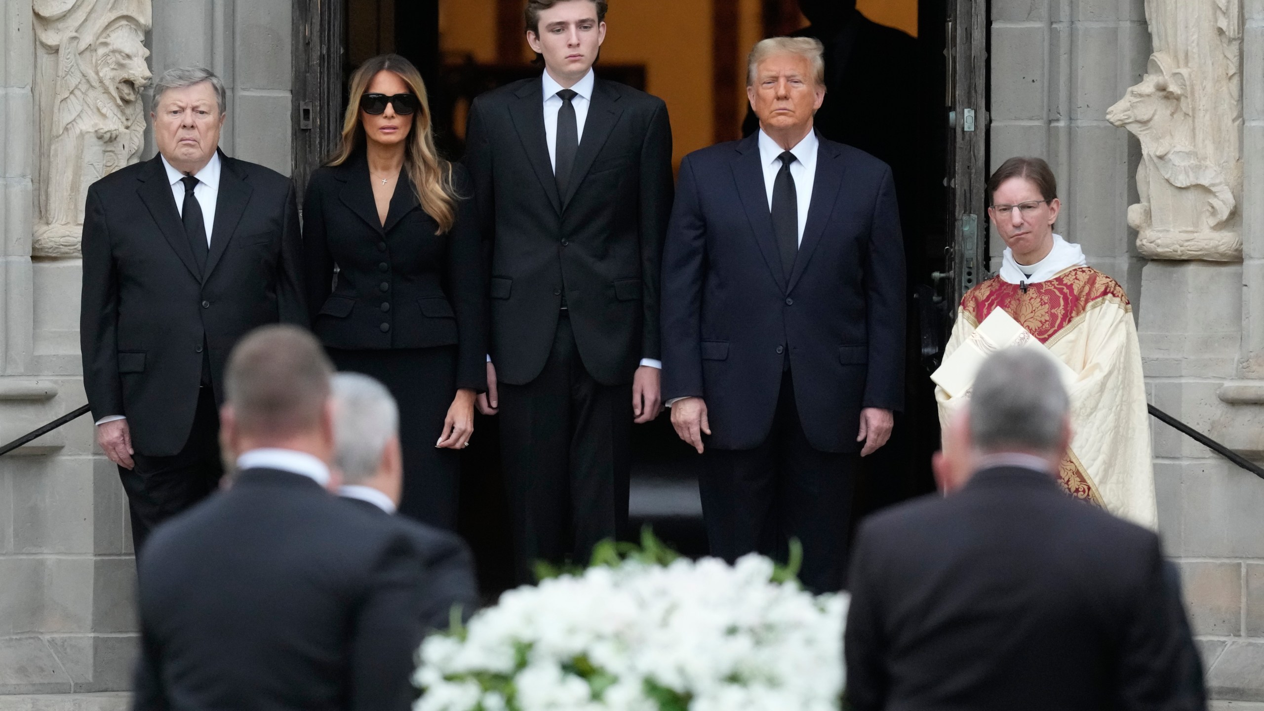 Former President Donald Trump, center right, stands with his wife Melania, second left, their son Barron, center left, and father-in-law Viktor Knavs, as the coffin carrying the remains of Amalija Knavs, the former first lady's mother, is carried into the Church of Bethesda-by-the-Sea for her funeral, Thursday, Jan. 18, 2024, in Palm Beach, Fla. (AP Photo/Rebecca Blackwell)