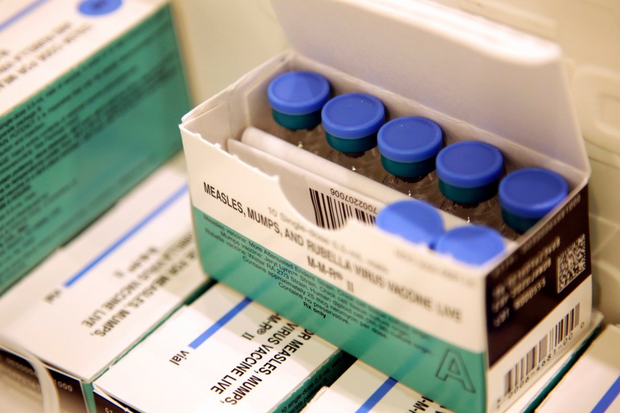 FILE- Vials of measles, mumps and rubella vaccine sit in a cooler at the Rockland County Health Department in Pomona, N.Y., March 27, 2019. A midwife on New York's Long Island, who gave nearly 1,500 children homeopathic pellets instead of required vaccinations, has been fined $300,000, the state's health department announced this week. (AP Photo/Seth Wenig, File)