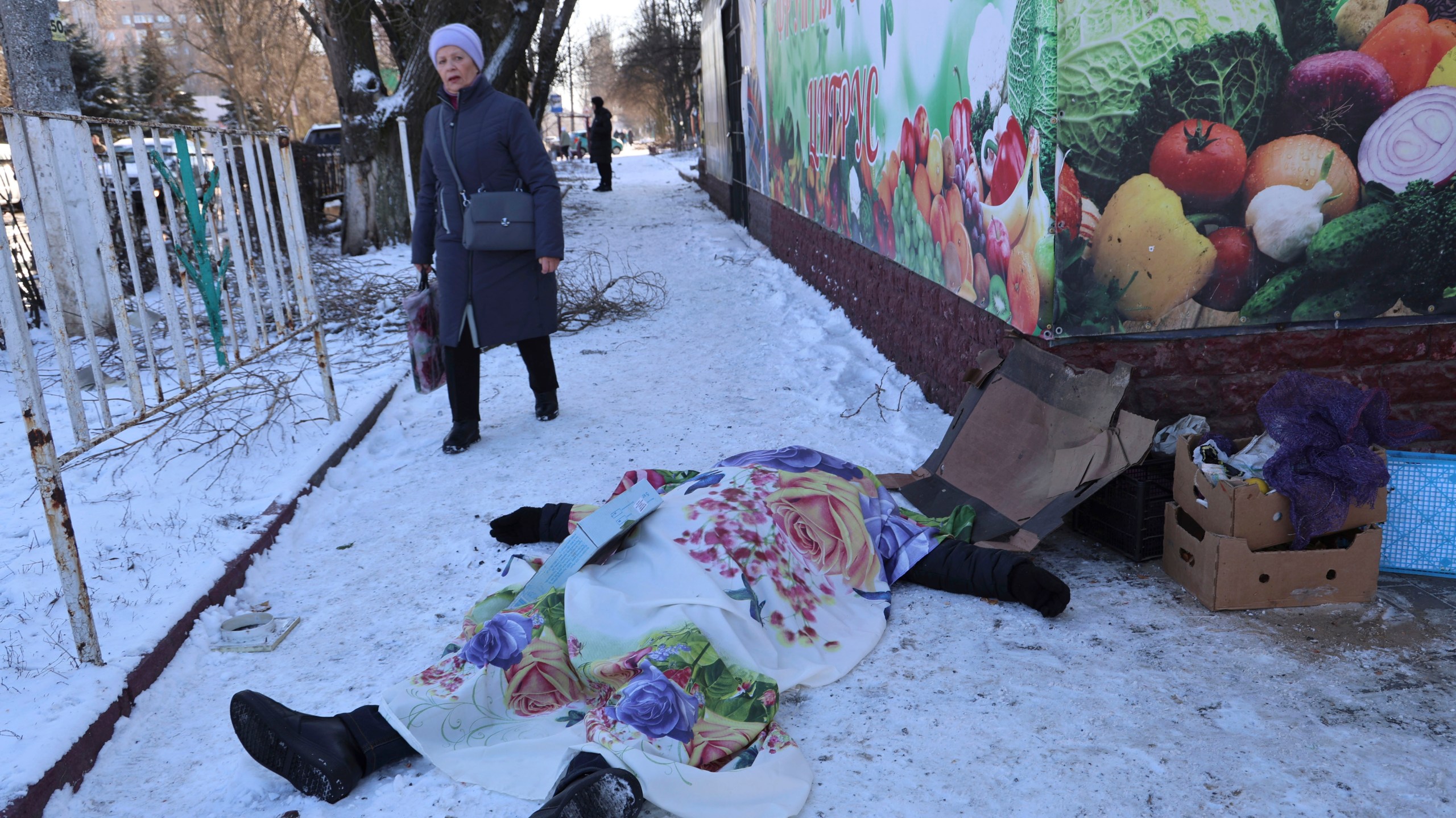 A woman walks past a body of a victim killed during the shelling that Russian officials in Donetsk said was conducted by Ukrainian forces, in Donetsk, Russian-controlled Donetsk region, eastern Ukraine in Donetsk, Ukraine, Sunday, Jan. 21, 2024. Local officials say at least 18 people have been killed by shelling of a market in Russian-occupied Ukraine. The attack hit Tekstilshchik, a suburb of the city of Donetsk, on Sunday. Alexei Kulemzin, the city's Russian-installed mayor, said that the shells had been fired by the Ukrainian military. (AP Photo/Alexei Alexandrov)