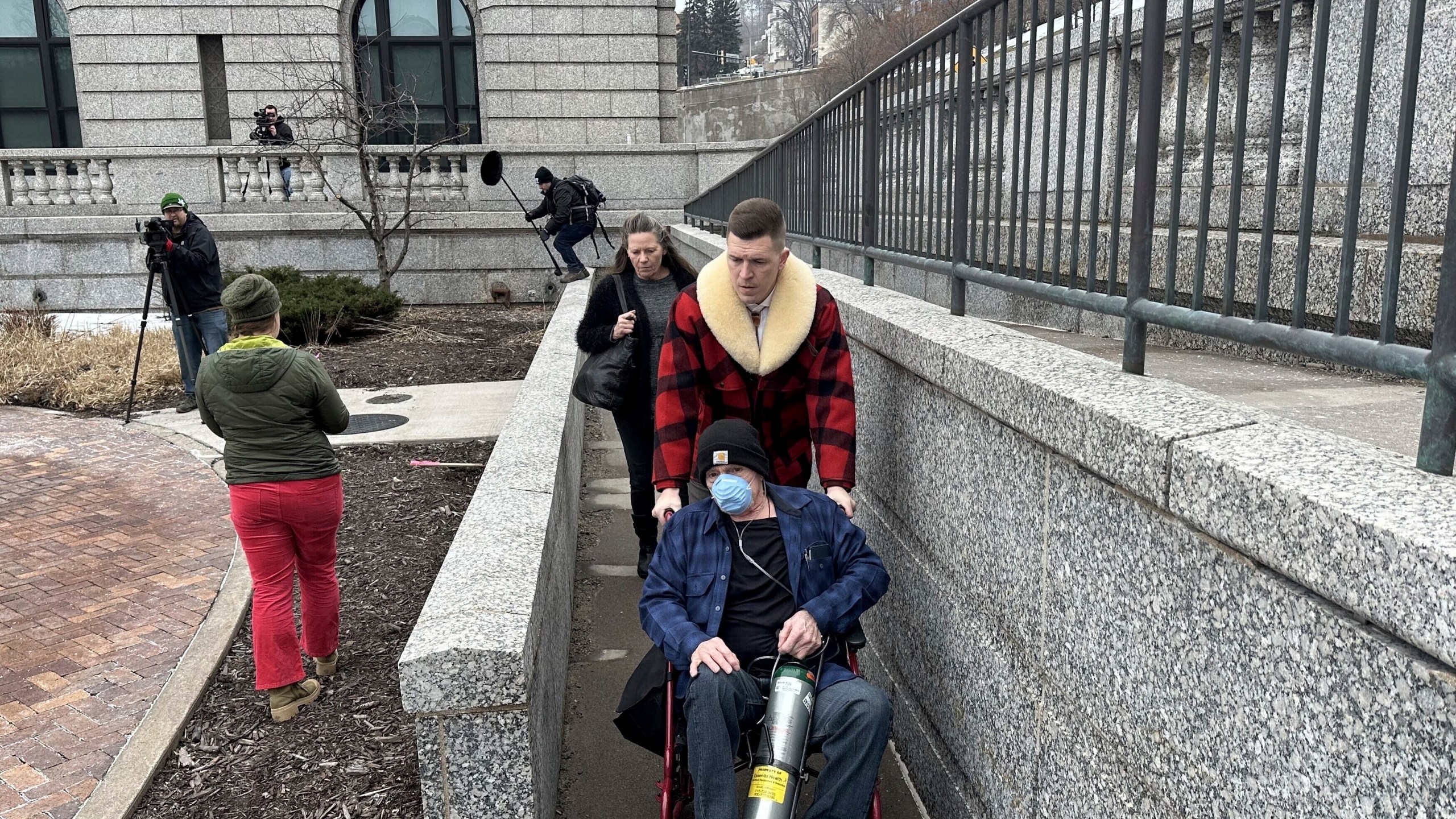 Terry Jon Martin, who pleaded guilty to stealing a pair of ruby red slippers worn by Judy Garland in "The Wizard of Oz," is wheeled out of the federal courthouse in Duluth, Minn. after his sentencing hearing on Monday, Jan. 29, 2024 by his attorney, Dane DeKrey. Martin, who is chronically ill and only has a couple months to live, will not have to serve time in prison for the crime. (Dan Kraker/Minnesota Public Radio via AP)