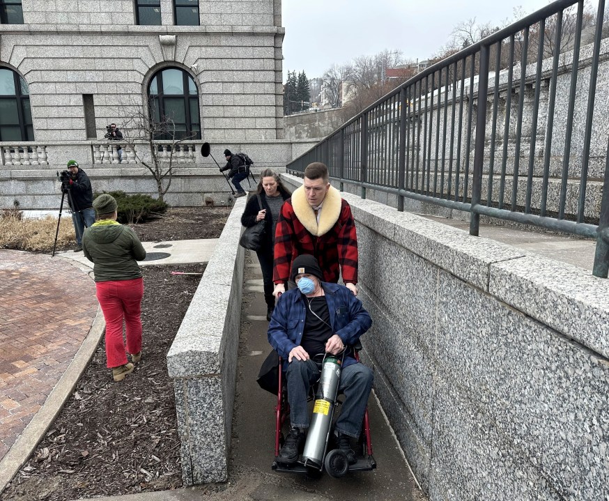 Terry Jon Martin, who pleaded guilty to stealing a pair of ruby red slippers worn by Judy Garland in "The Wizard of Oz," is wheeled out of the federal courthouse in Duluth, Minn. after his sentencing hearing on Monday, Jan. 29, 2024 by his attorney, Dane DeKrey. Martin, who is chronically ill and only has a couple months to live, will not have to serve time in prison for the crime. (Dan Kraker/Minnesota Public Radio via AP)