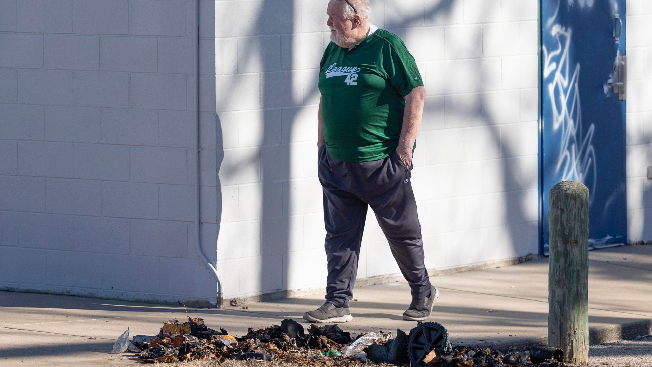 Bob Lutz, the executive director of League 42, a youth baseball league in Wichita, Kan., walks past the charred remains of a trash dumpster where pieces of a stolen Jackie Robinson statue were found by Wichita police on Tuesday, Jan. 30, 2024. The life-sized statue of baseball pioneer Jackie Robinson was cut off at the ankles from the League 42 baseball field on January 25th. Police have made no arrests in the case but said Tuesday that the statue was damaged beyond repair. (Travis Heying/The Wichita Eagle via AP)