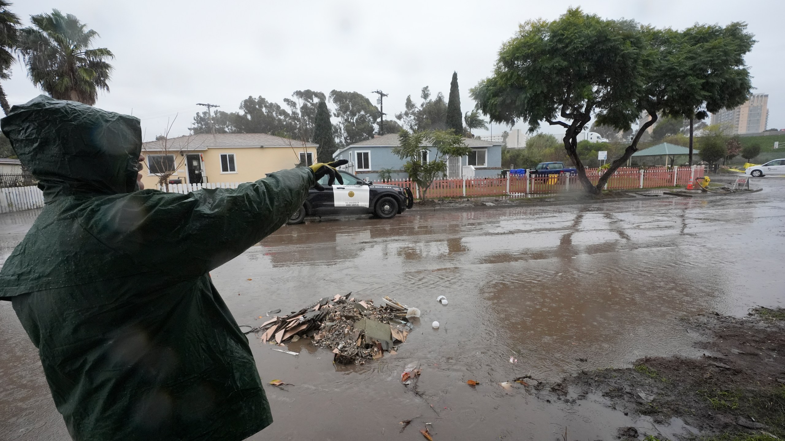 Ruben Gomez points along a partially flooded street as he breaks from clearing away mud and flood debris that engulfed his parents' home in the previous rainstorm as more rain falls Thursday, Feb. 1, 2024, in San Diego. Gomez has spent all of his time since the Jan. 22 storm shuttling between caring for his parents who were rescued by boat and later hospitalized that day, and trying to salvage what he can from the flooded home. Now, with more rain coming, Gomez worries the floodwaters may rise again in his parents' neighborhood. (AP Photo/Gregory Bull)