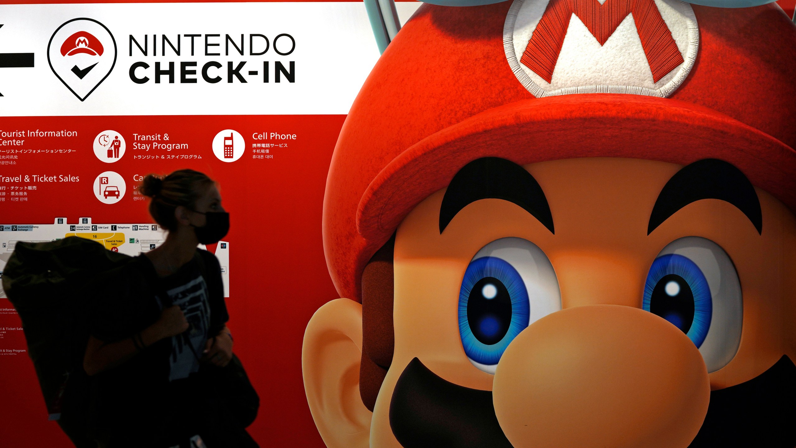 FILE - A traveler walks past an advertisement featuring a Nintendo character at Narita airport in Narita near Tokyo on June 10, 2022. Nintendo has reported healthy sales and profits on the back of the hit “Super Mario Bros. Wonder” game, prompting the Japanese video game maker to raise its full fiscal year forecasts. (AP Photo/Shuji Kajiyama, File)