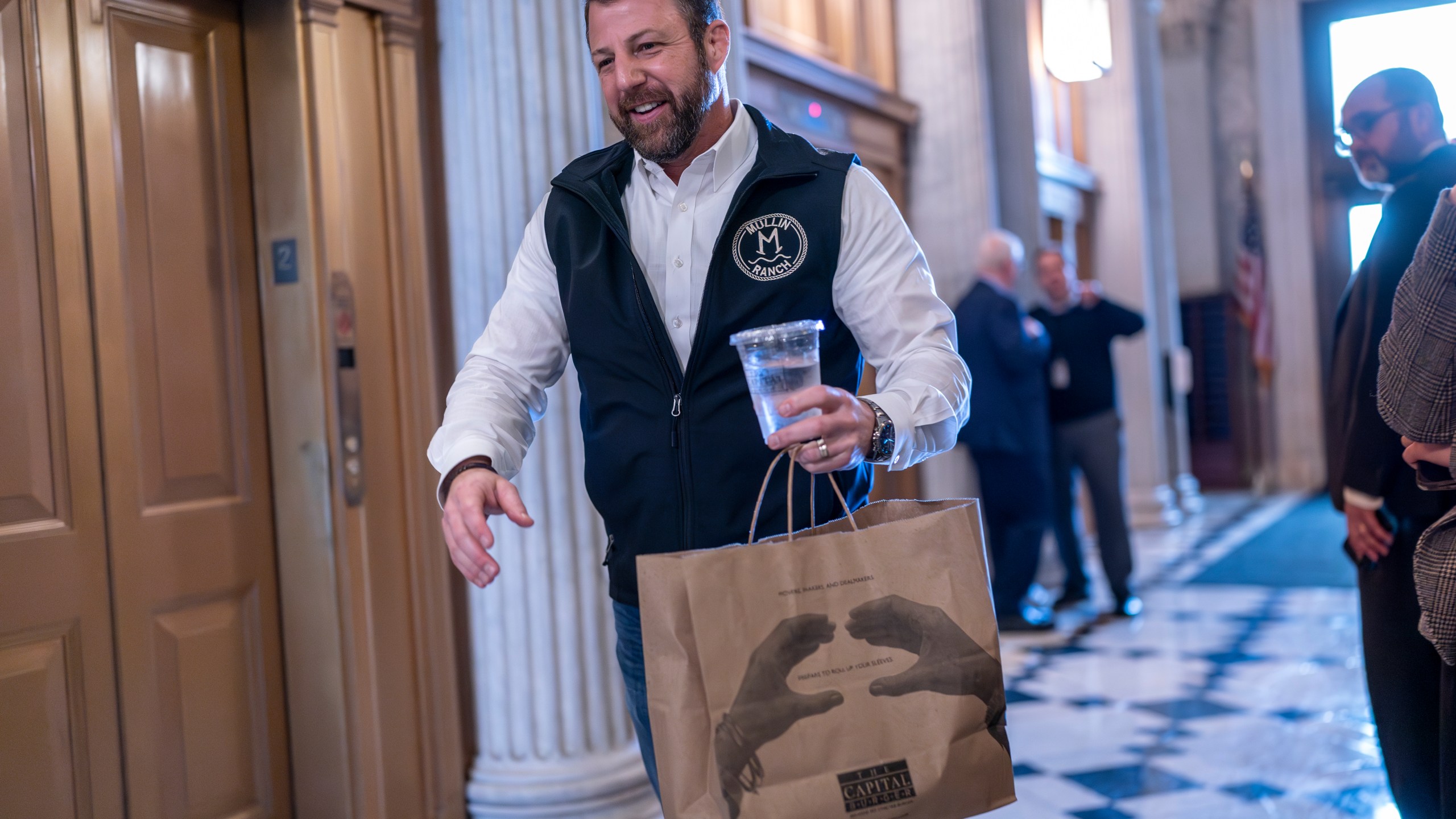 Sen. Markwayne Mullin, R-Okla., arrives with a carryout bag of hamburgers as the Senate prepares a procedural vote on an emergency spending package that would provide military aid to Ukraine and Israel, replenish U.S. weapons systems and provide food, water and other humanitarian aid to civilians in Gaza, at the Capitol in Washington, Sunday, Feb. 11, 2024. (AP Photo/J. Scott Applewhite)